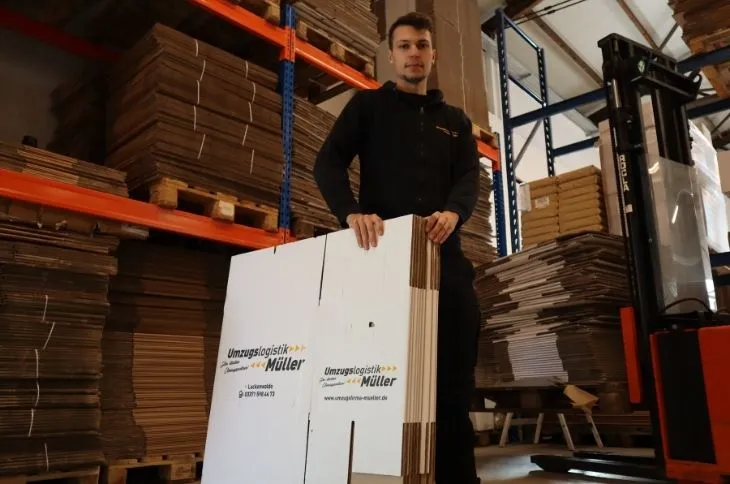 umzugshelfer haelt flach zusammengelegte umzugskartons im lager